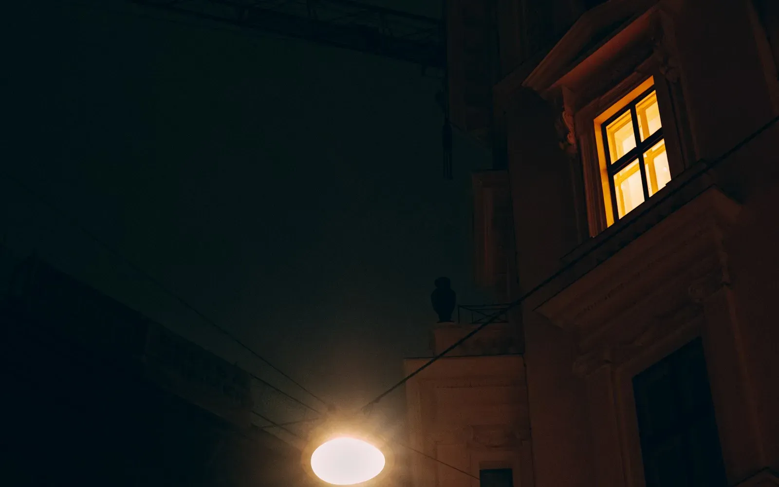 Erleuchtetes Fenster an einer Hausfassade bei Nacht, darunter eine Straßenlaterne