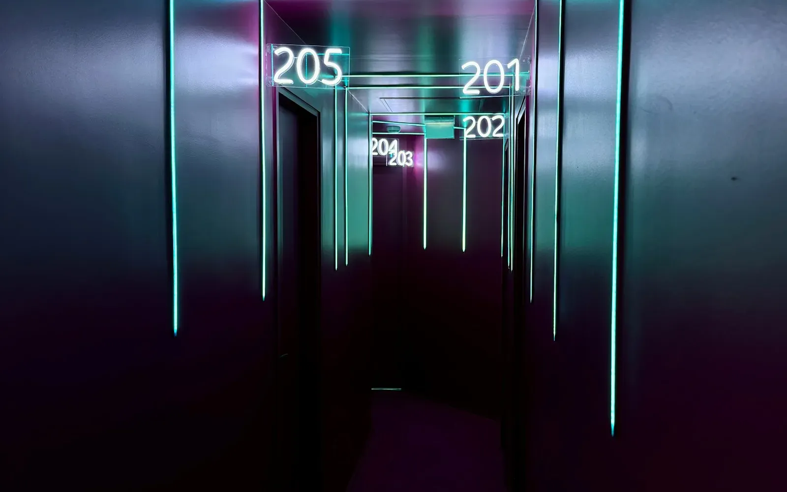 Schmaler Flur mit Neonlicht und leuchtenden Zimmernummern an den Türen