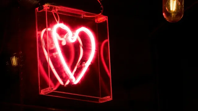 Rot leuchtendes Neonherz in einem Glaskasten vor dunklem Hintergrund – Kaufmich oder Ladies im Vergleich
