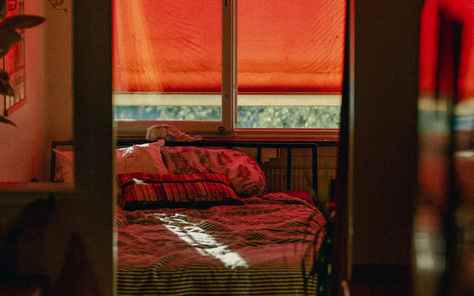 Blick durch eine Tür in ein Schlafzimmer mit rotem Rollo und gemachtem Bett