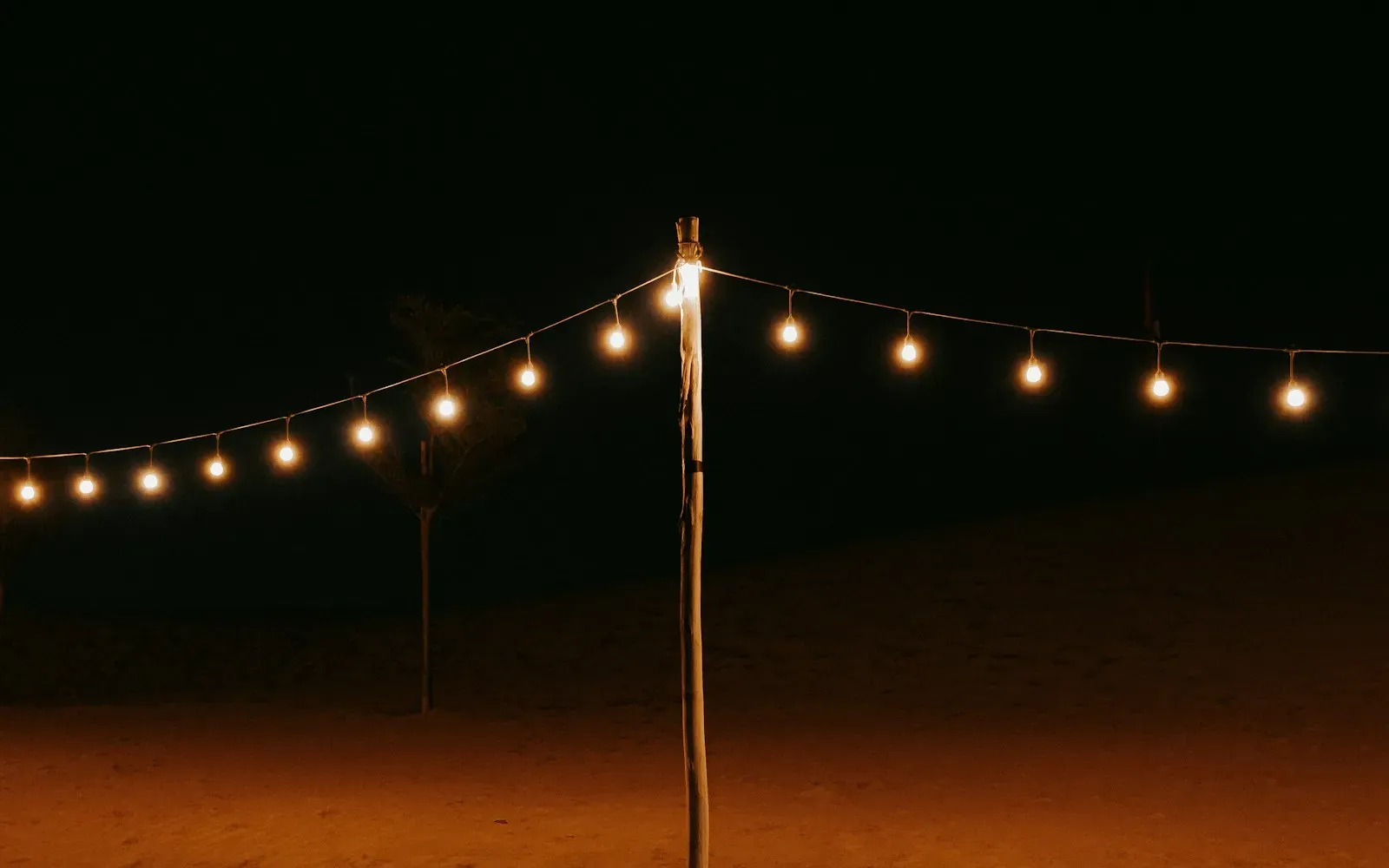 Lichterkette zwischen Holzpfählen an einem nächtlichen Sandstrand